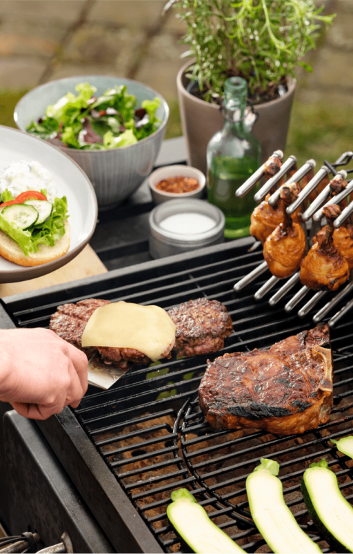 Burgery, udka z kurczaka na stojaku do pokrywek i kotlety na grillu.